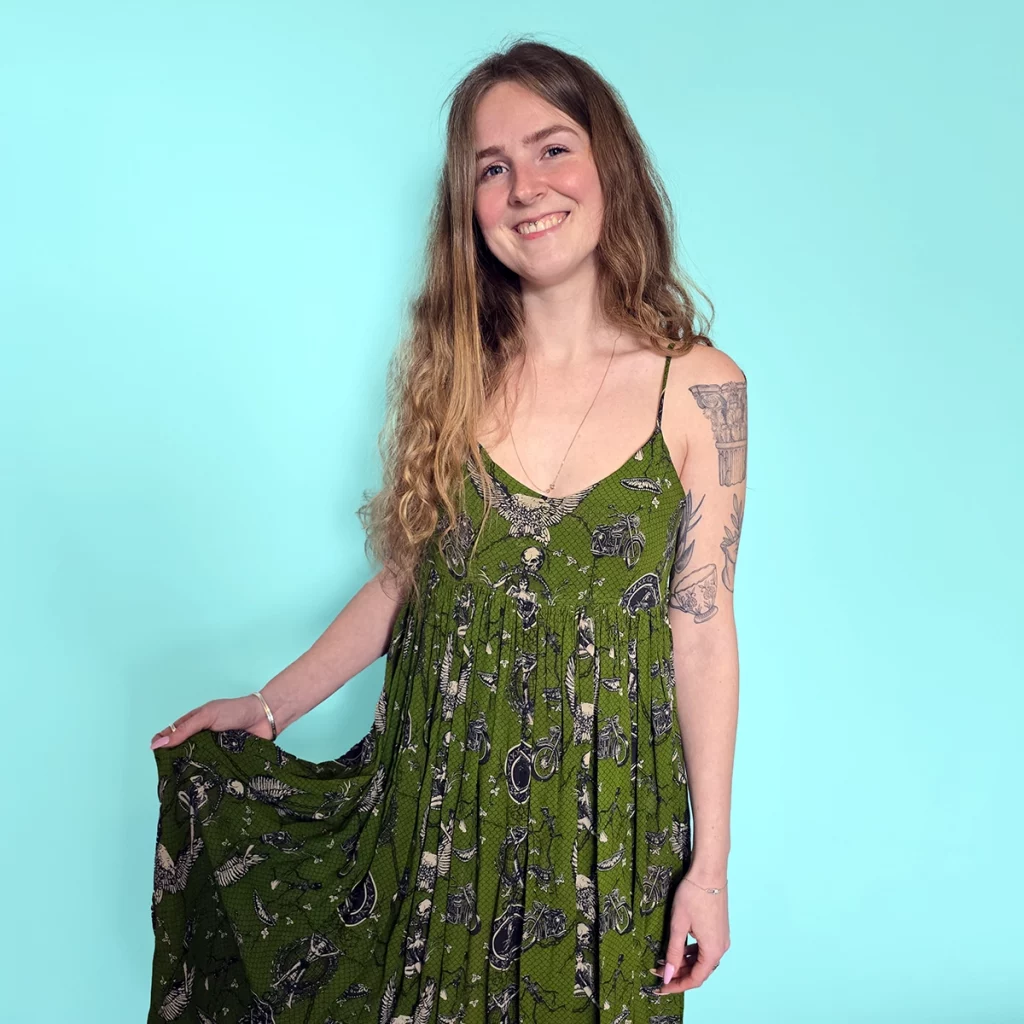 Young woman with tattoos wearing a green dress with illustrations of skeletons and motorcycles 