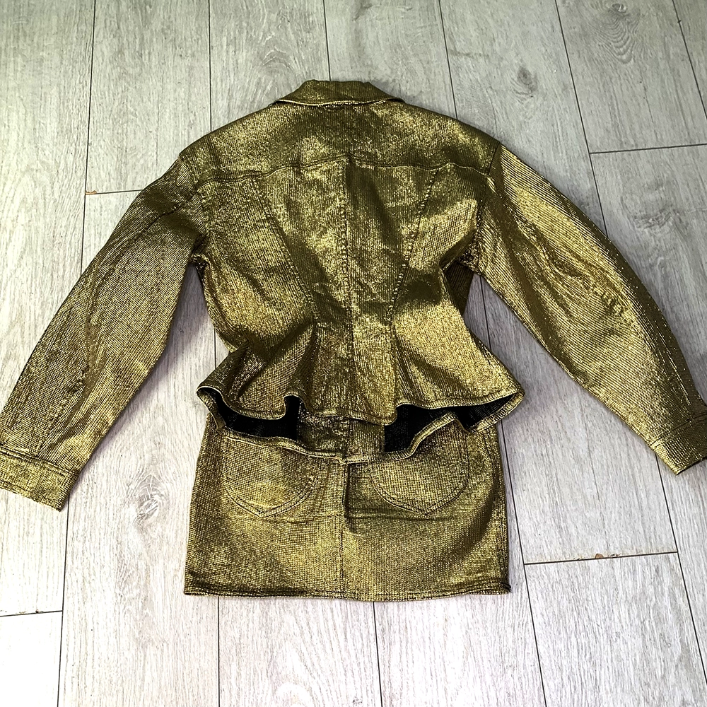 The back of a gold lame skirt and peplum jacket on top of light wooden floorboards.