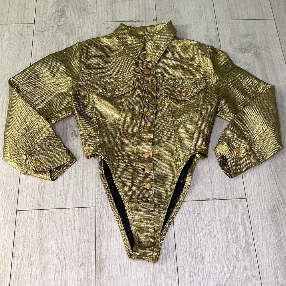 The front of a gold lame bodysuit on top of light wooden floorboards.