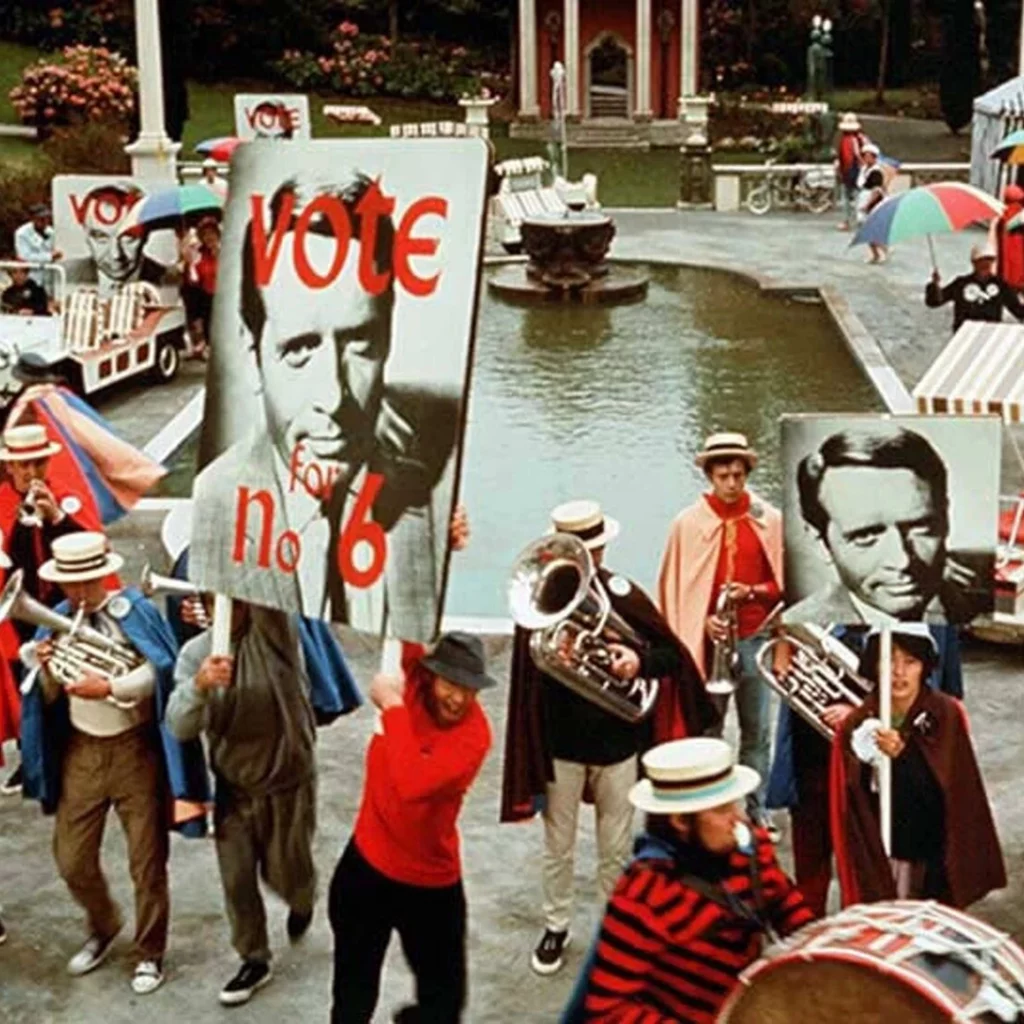 A scene from The Prisoner episode with actors holding placards reading Vote for No 6.