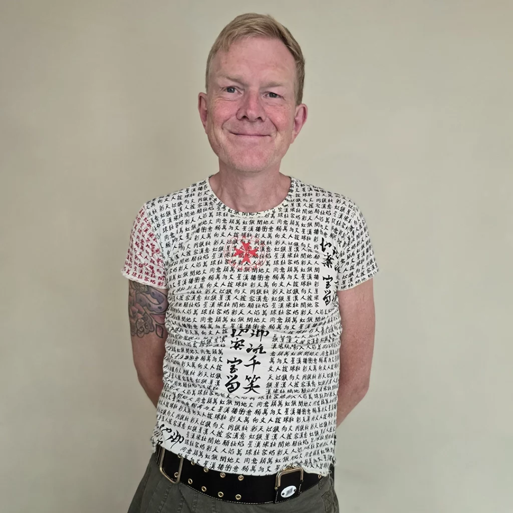 Person standing in front of off white wall wearing t-shirt with Japanese writing on