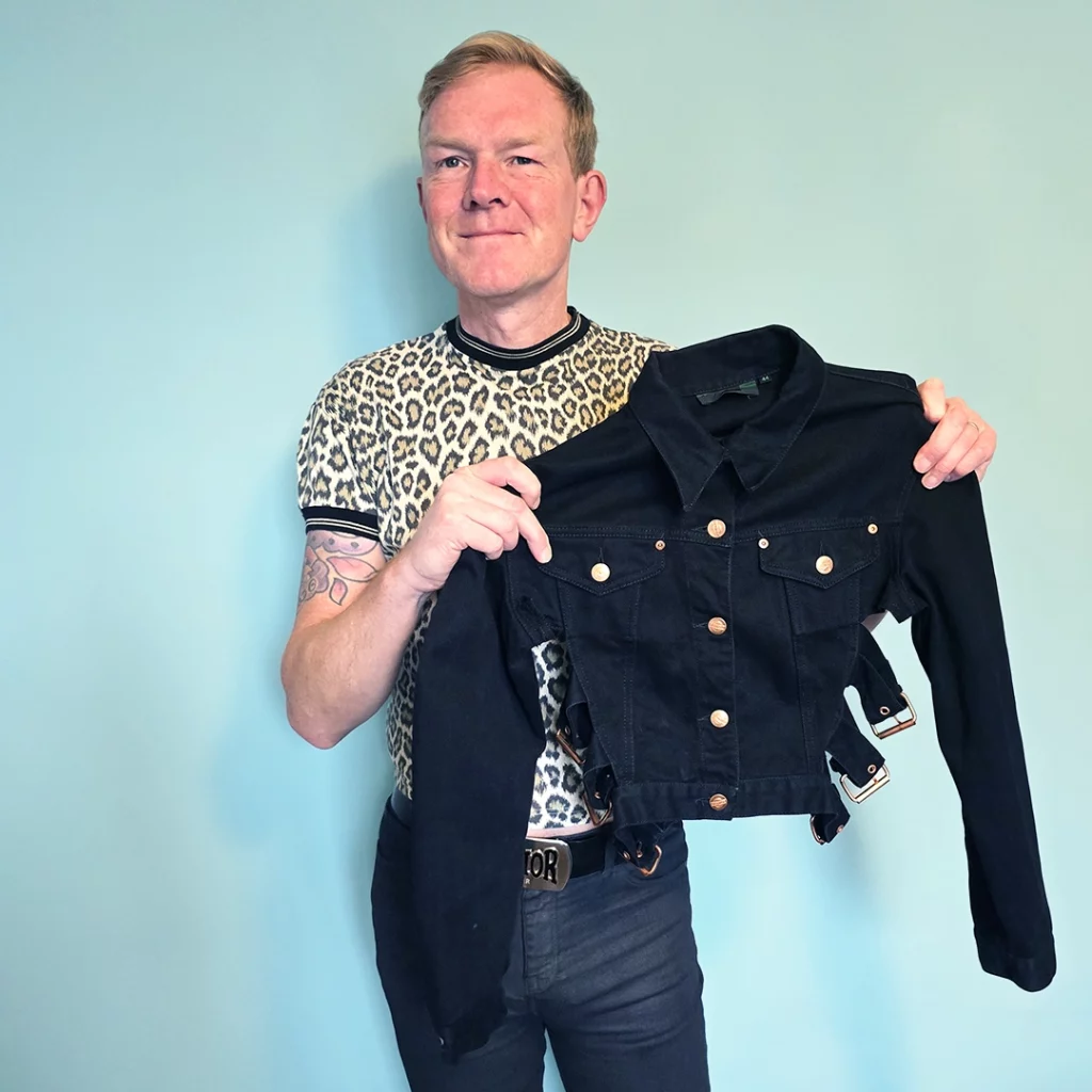A man holding a denim jacket with side buckles.