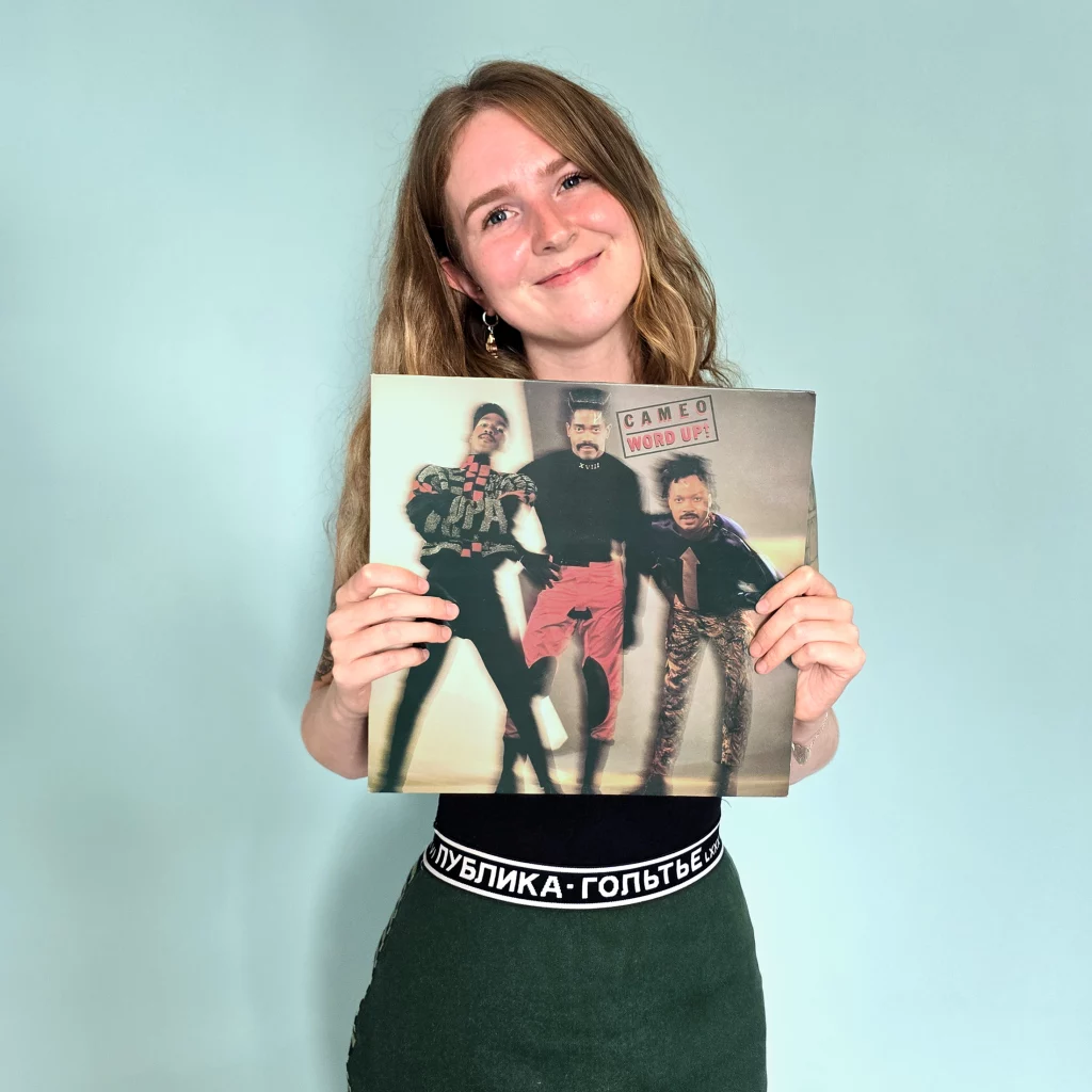 Woman wearing a skirt with Russian lettering and holding a record with cameo on the cover 