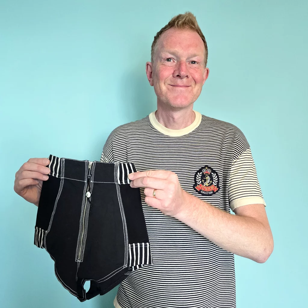 Man holding a pair of hot pants with a zip front.